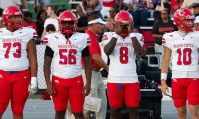 Four football players in red and white uniforms stand on the sidelines during a game. — Warren Central district play