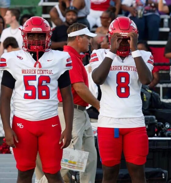 Four football players in red and white uniforms stand on the sidelines during a game. — Warren Central district play