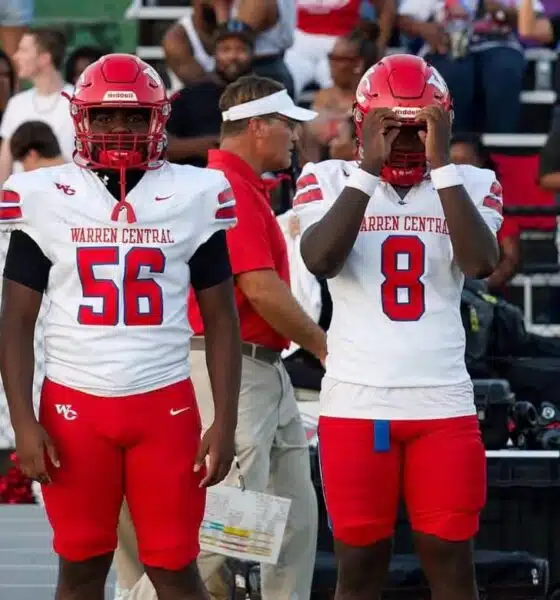 Four football players in red and white uniforms stand on the sidelines during a game. — Warren Central district play