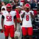 Four football players in red and white uniforms stand on the sidelines during a game. — Warren Central district play