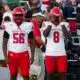 Four football players in red and white uniforms stand on the sidelines during a game. — Warren Central district play