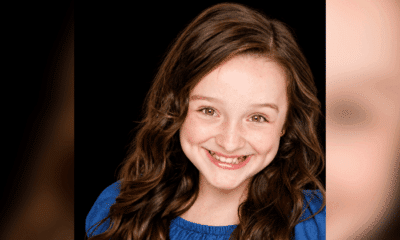 Elvie Grace smiles in a blue top in a studio portrait with a dark background.