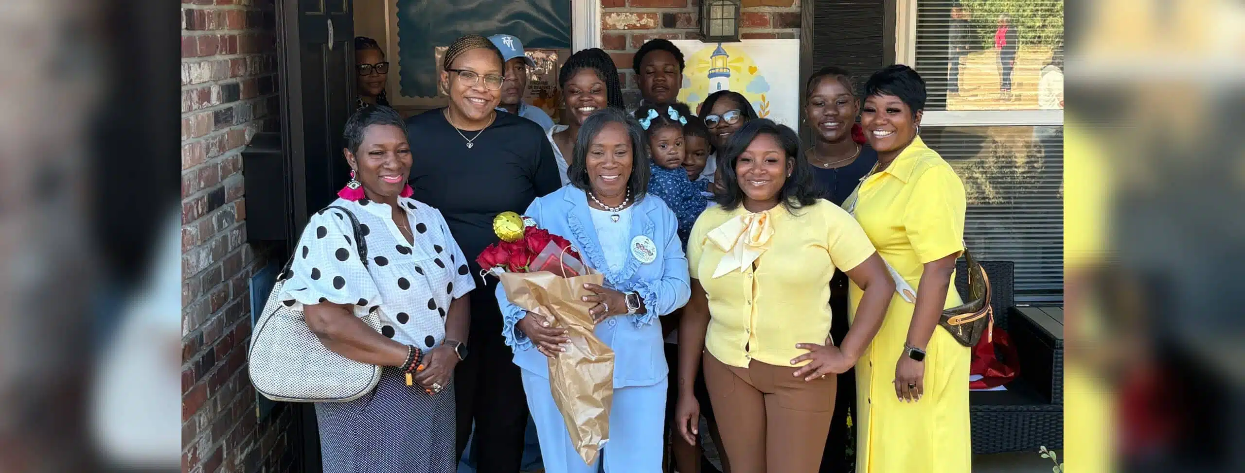 Group of people celebrating the opening of Guiding Light Early Learning Center with Sylvia Brown at the center holding flo…