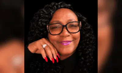 A woman with curly hair and glasses smiles, showcasing her long red nails and a ring. — Stephanie Cherey Jones