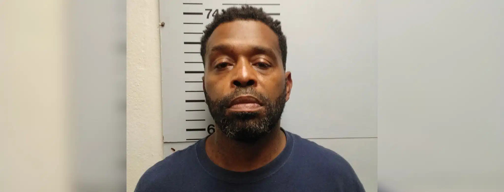 Mugshot of a man with short hair and a beard, wearing a blue shirt, against a height chart background. — Side by side