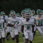 Vicksburg Gators football team running onto the field in white uniforms during a game.