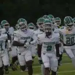Vicksburg Gators football team running onto the field in white uniforms during a game.
