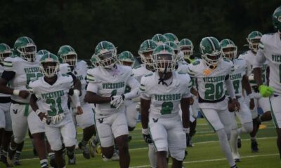 Vicksburg Gators football team running onto the field in white uniforms during a game.
