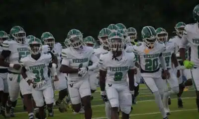 Vicksburg Gators football team running onto the field in white uniforms during a game.