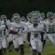 Vicksburg Gators football team running onto the field in white uniforms during a game.
