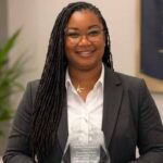 Kimberley King smiles in a dark blazer and white blouse, holding an award plaque.
