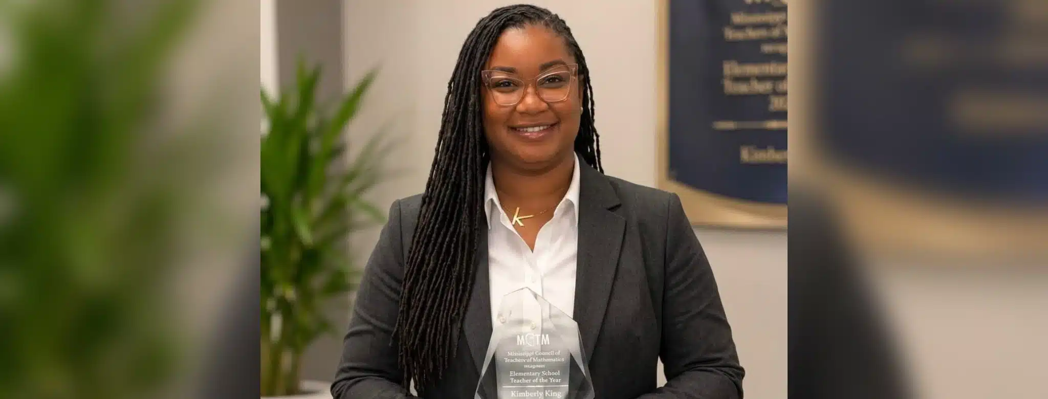 Kimberley King smiles in a dark blazer and white blouse, holding an award plaque.