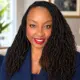 Portrait of Dr. Kim Carter Evans with long braided hair, wearing a navy blazer and red lipstick, smiling confidently.
