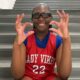Pharrah Moody in a red Lady Vikes basketball jersey and glasses, smiling and gesturing on gym bleachers