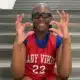 Pharrah Moody in a red Lady Vikes basketball jersey and glasses, smiling and gesturing on gym bleachers