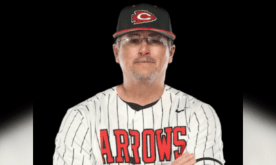 A coach in a striped baseball jersey and cap, representing Hinds Athletics, poses confidently with arms crossed.