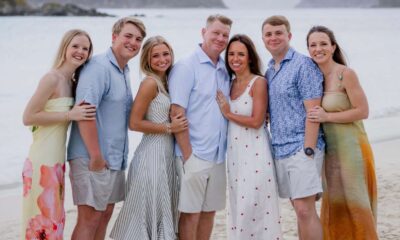 The Larsen family stands together on a beach, smiling in summer clothing.