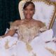 A young woman in an ornate white-and-gold gown sits on a throne-style chair beside black and gold balloons. — Milah Davis