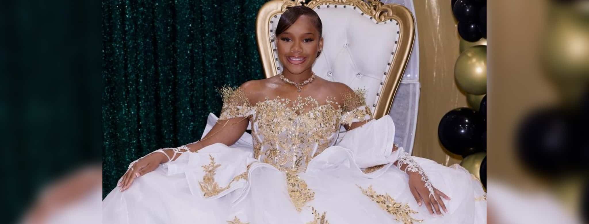 A young woman in an ornate white-and-gold gown sits on a throne-style chair beside black and gold balloons. — Milah Davis
