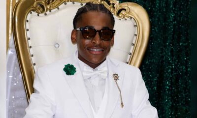 Cameron Pickett in a white suit and sunglasses seated in an ornate chair