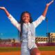 Addison Anderson poses with arms raised on a track in front of a stadium on a sunny day.