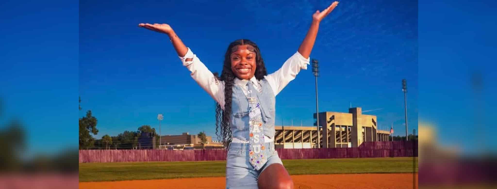 Addison Anderson poses with arms raised on a track in front of a stadium on a sunny day.