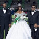 Raylyn Parson homecoming queen in a white gown, standing with family on the football field