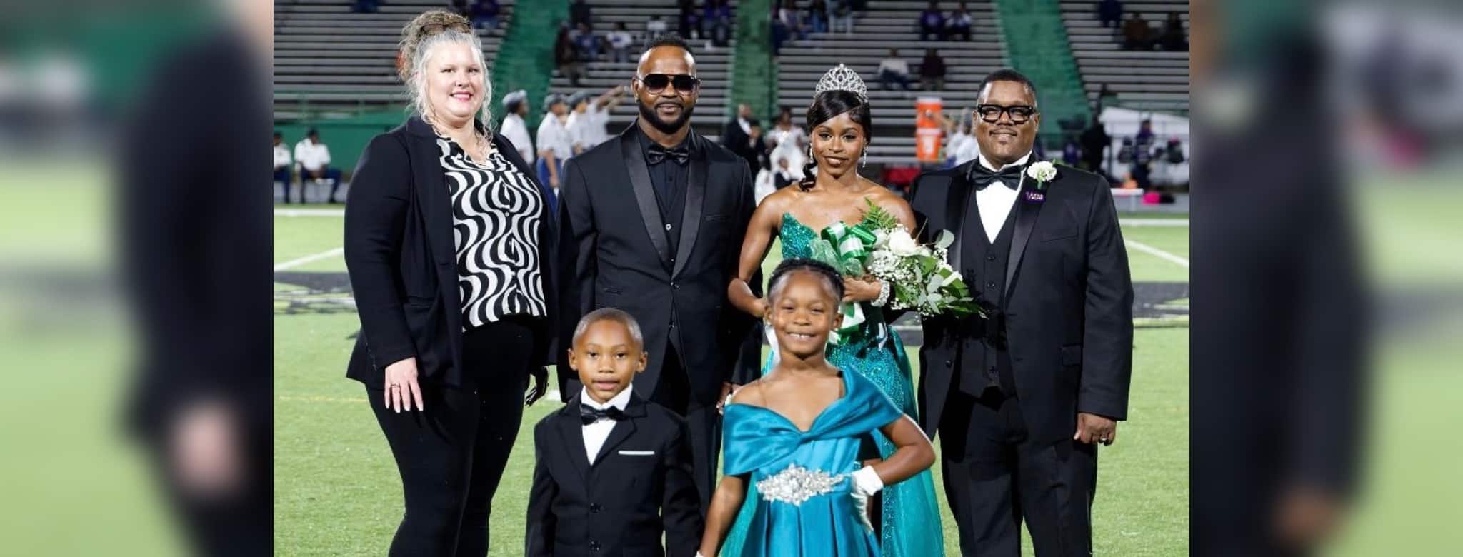 To’Nia Taylor homecoming queen in a turquoise gown poses with family members on the football field.