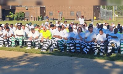 About 300 inmates in striped uniforms and white shirts sit in rows outdoors for a graduation ceremony.