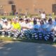 About 300 inmates in striped uniforms and white shirts sit in rows outdoors for a graduation ceremony.